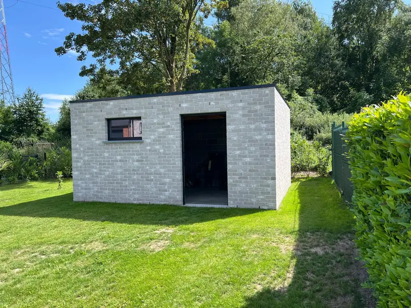 Abri de jardin maçonné en blocs de parement gris, avec linteau et baie
