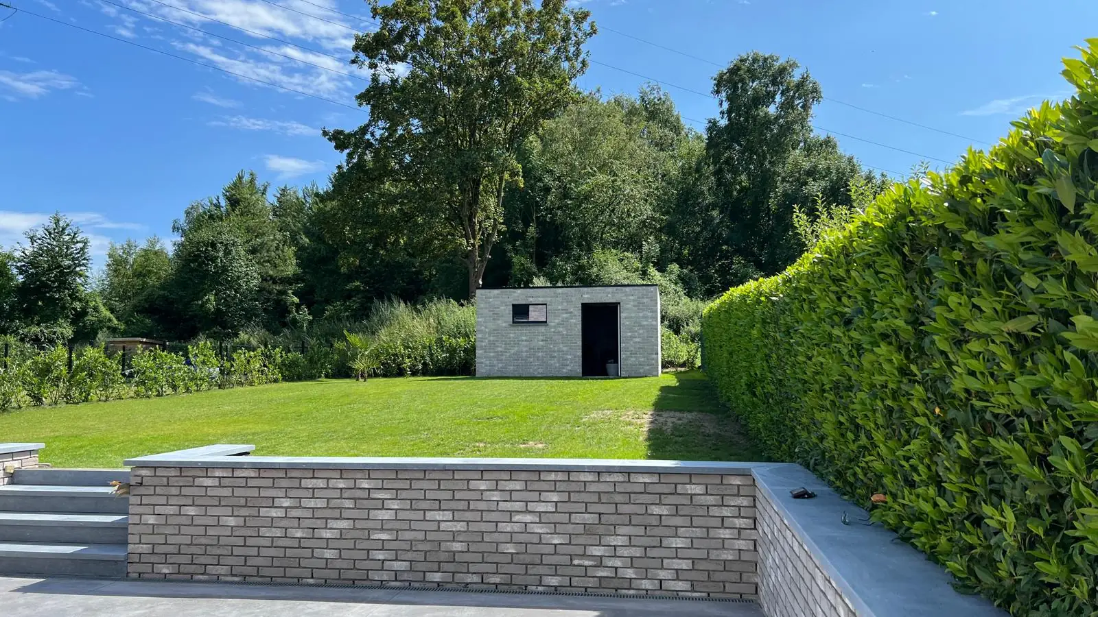 Jardin en pente retenu par un mur de soutènement en brique, avec terrasse en béton lissé
