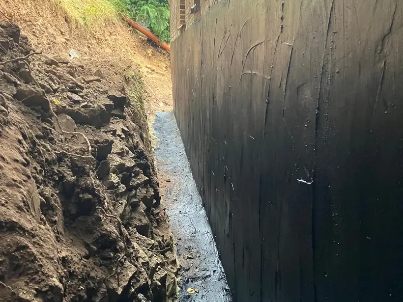 Membrane d'étanchéité noire appliquée sur un mur contre terre avant remblai