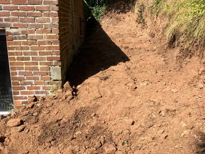 Terre décaissée le long d'un mur en brique pour dégager la partie enterrée