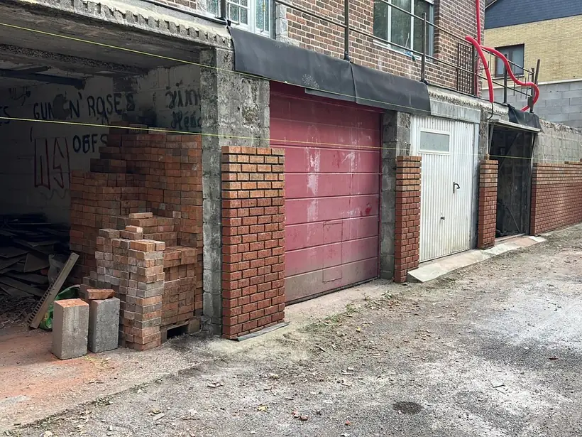 Mur de façade dégradé et abords de garages encombrés, avant intervention