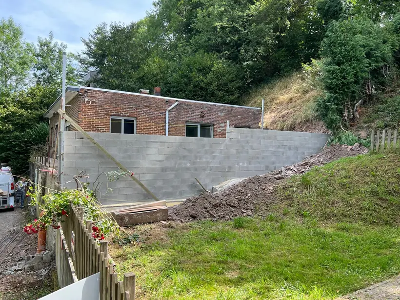 Le talus décaissé et retenu par un mur de soutènement en blocs béton, avec dalle en pied
