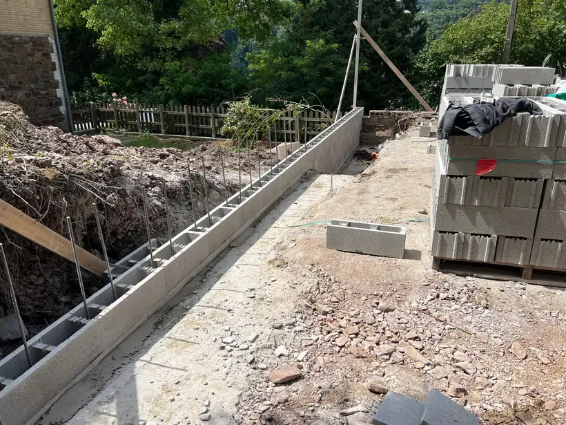 Tranchée de fondation armée le long d'une allée, blocs béton livrés à côté